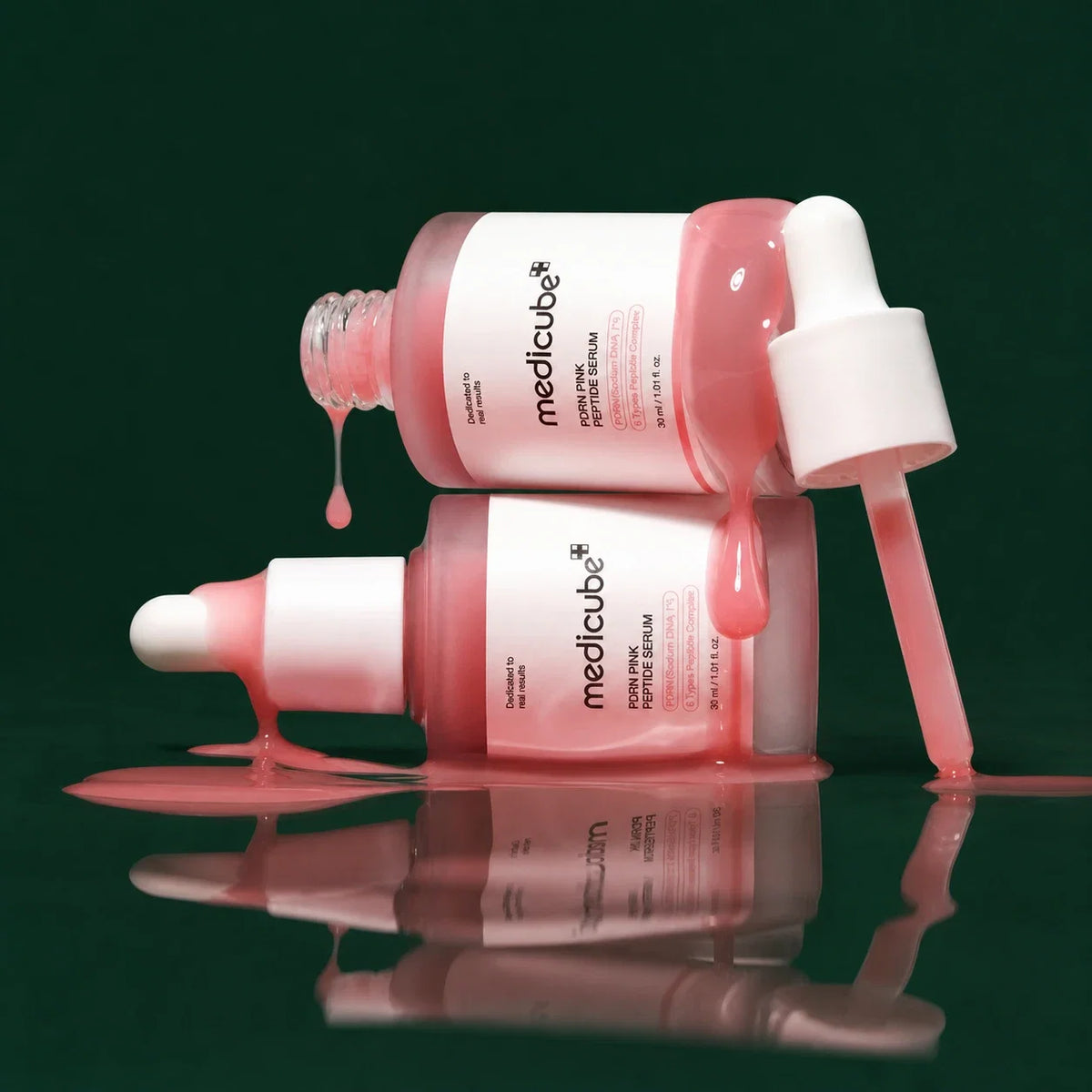 Medicube Ampoule PDRN Rose et Peptides, deux flacons et texture rose sur fond vert profond