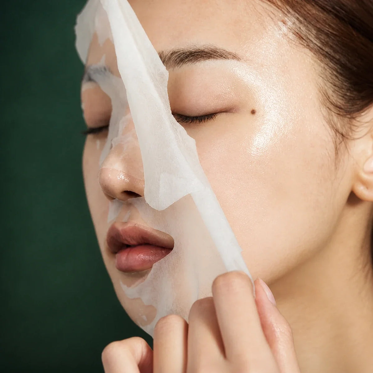 Masque tissu Super Cica Medicube retiré du visage sur fond vert profond