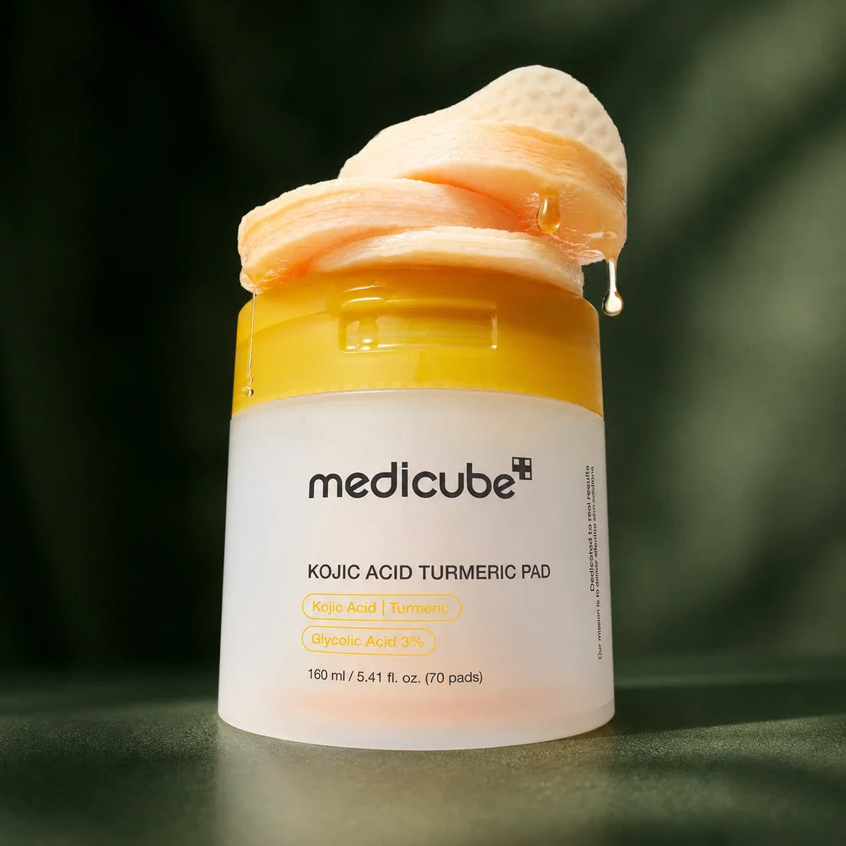 Texture des pads Medicube Kojic Acid Turmeric sur fond vert profond